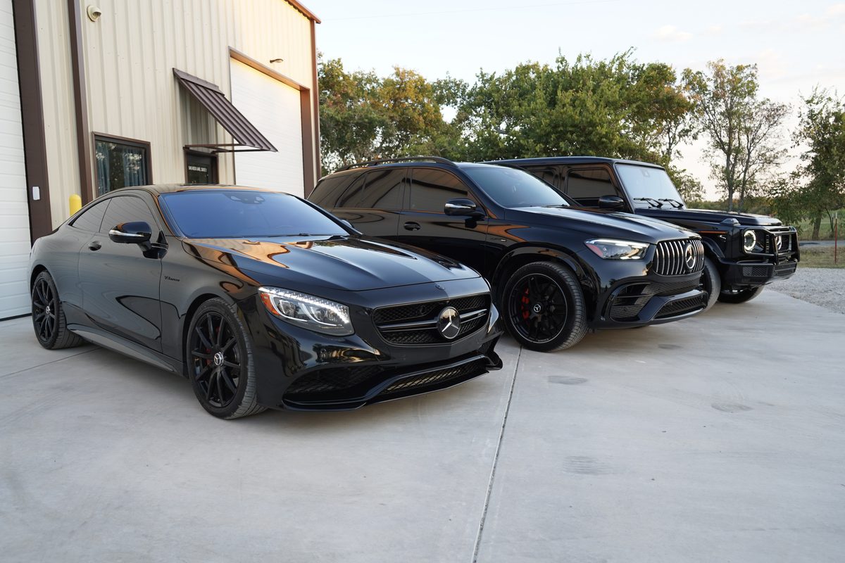 A Mercedes-Benz S-Class coupe leading a line of vehicles outside the shop in warm evening light